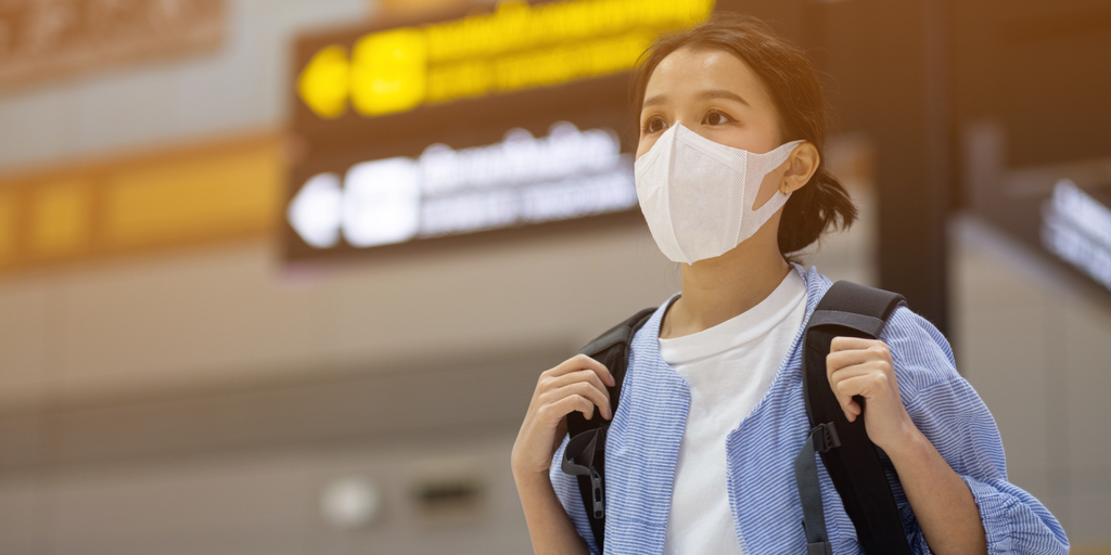 air traveler wearing mask in front of departures sign